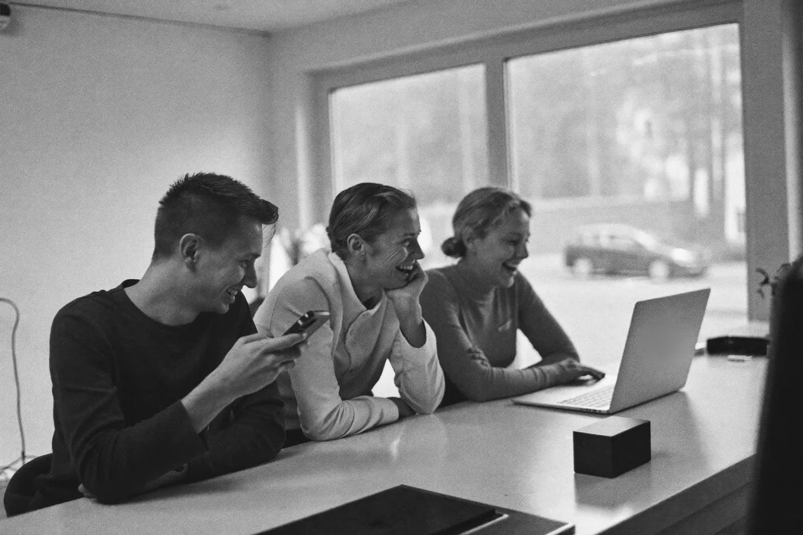 Equipo pequeño riendo mientras revisa conversaciones en el portátil y el móvil